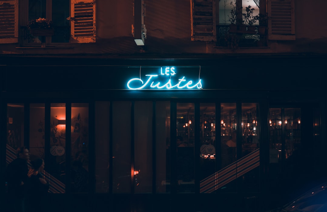 Façade d'un restaurant parisien de nuit avec une enseigne néon bleu "Les Justes" — illustration néon verre vs néon LED flex