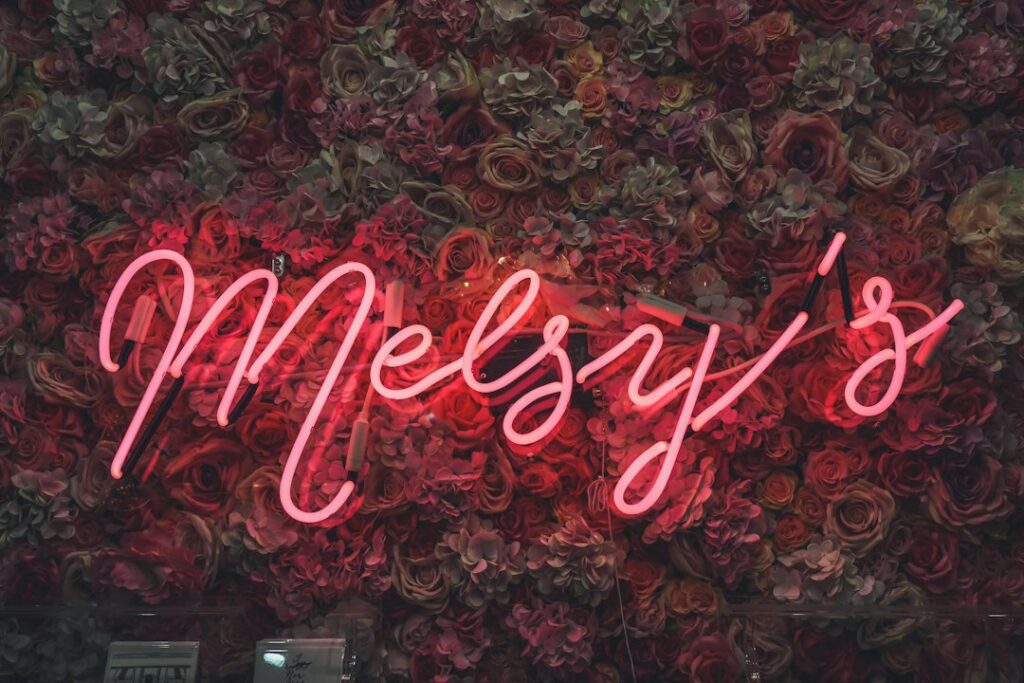 Néon LED rose avec un prénom en écriture cursive sur un mur de fleurs