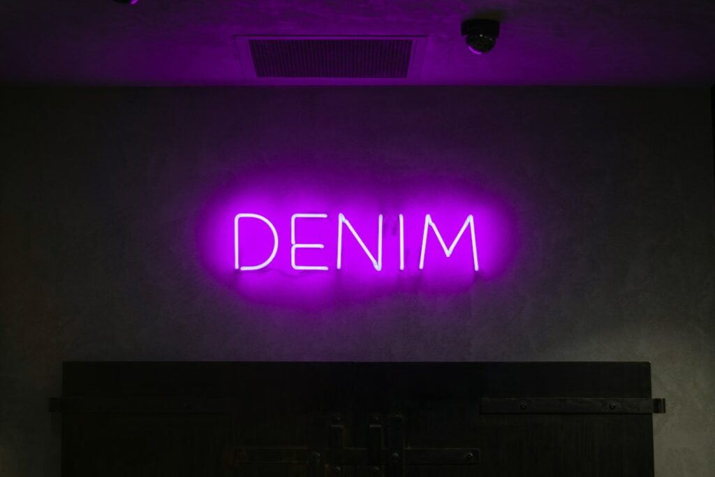 Enseigne néon LED violette avec inscription DENIM montée sur mur sombre en boutique retail