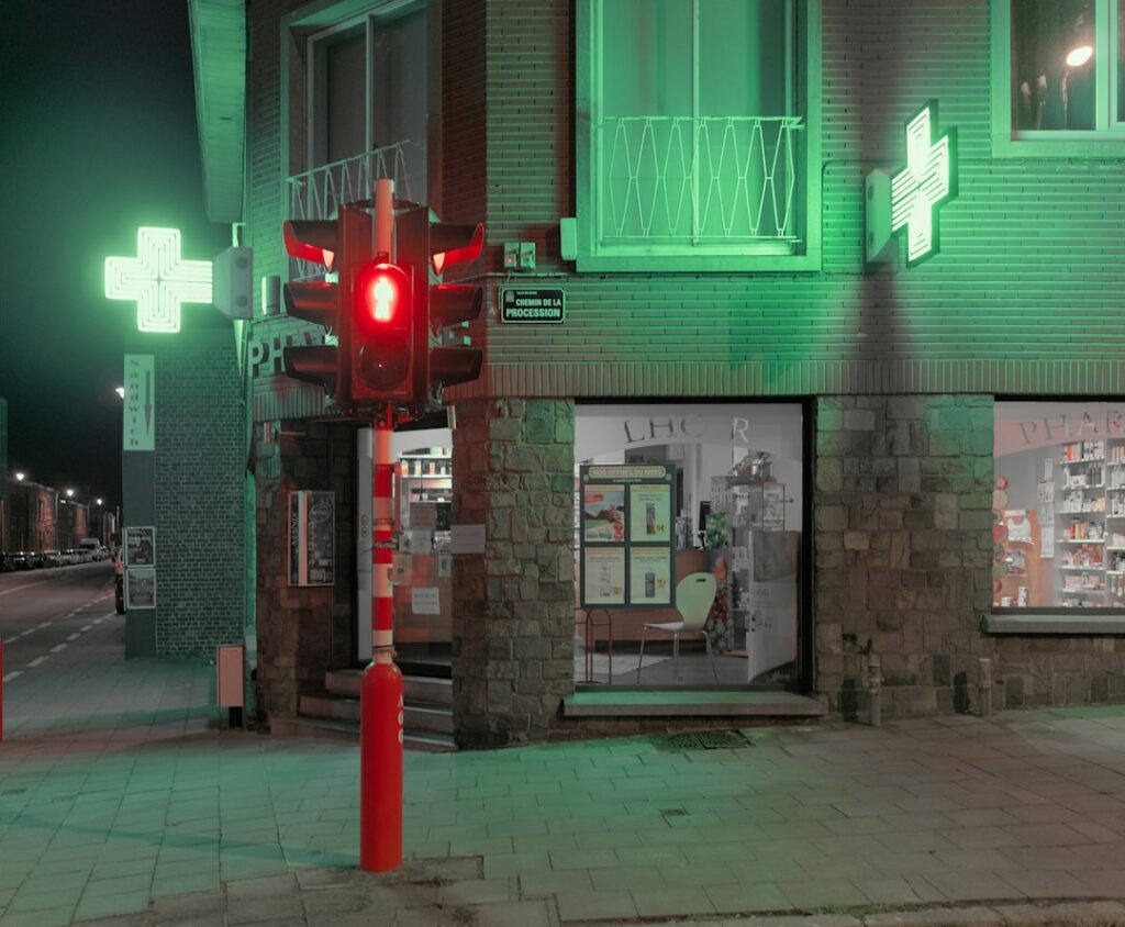 Officine en angle de rue avec deux croix vertes lumineuses visibles la nuit, illustrant la double face et la visibilité depuis la voie publique