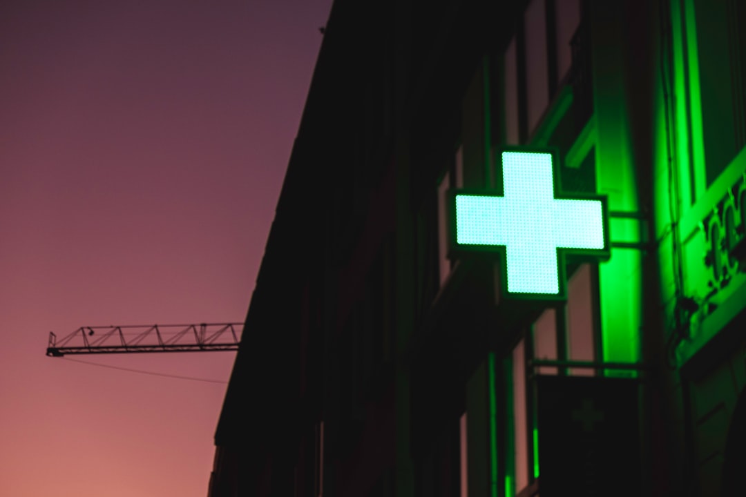 Croix verte lumineuse de pharmacie illuminée sur façade urbaine au crépuscule