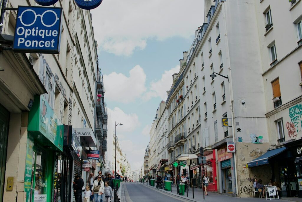 Rue commerçante parisienne avec enseigne drapeau perpendiculaire visible depuis le trottoir, illustrant la visibilité bilatérale pour les piétons